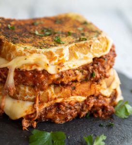 two sandwiches stacked on each other with bolognese and cheese spilling out
