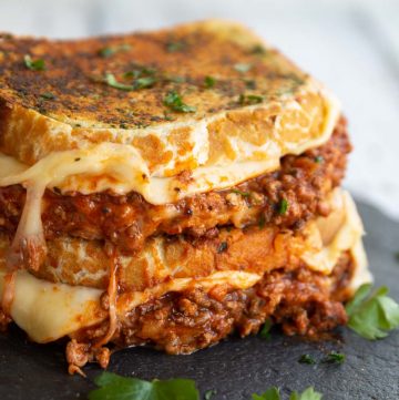 two sandwiches stacked on each other with bolognese and cheese spilling out