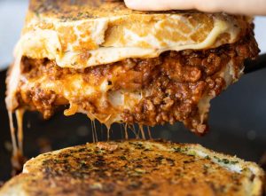 pulling grilled cheese out of pan with bolognese and cheese spilling out