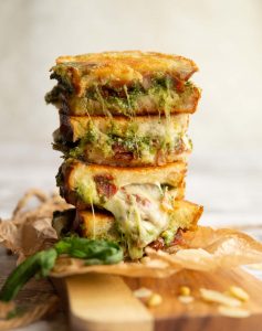 4 sandwich halves stacked on top of each other with pesto and cheese spilling out