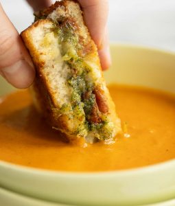 dunking grilled cheese into soup in green bowl