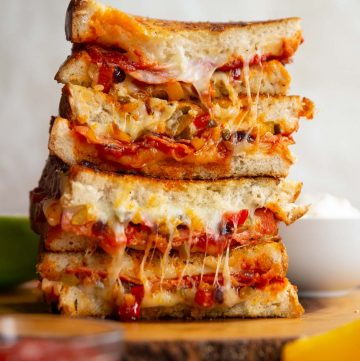 4 sandwich halves stacked on each other with cheese and filling spilling out