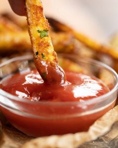 close up shot of single fry being dunked into small pot of ketchup