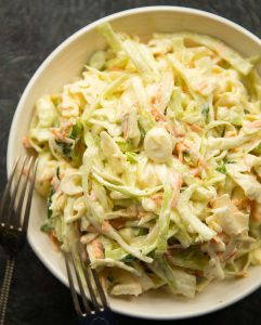 overhead shot of coleslaw in white bowl with two silver forks resting on it