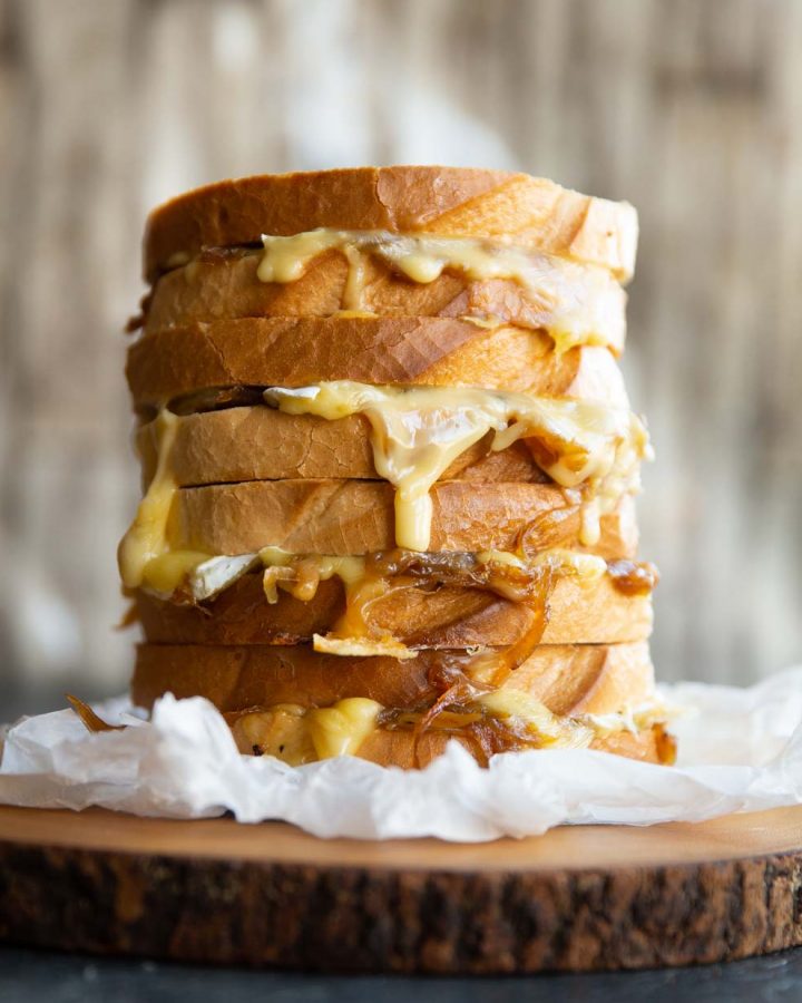 4 grilled cheeses stacked on each other on wooden board with cheese dripping out