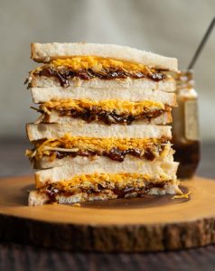 4 sandwich halves stacked on each other on wooden board with jar of pickle behind