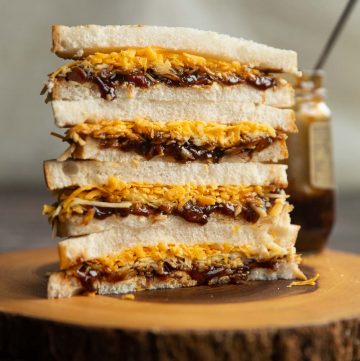 4 sandwich halves stacked on each other on wooden board with jar of pickle behind