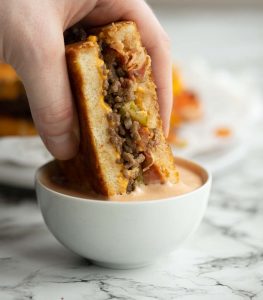dunking halves a grilled cheese into small pot of burger sauce