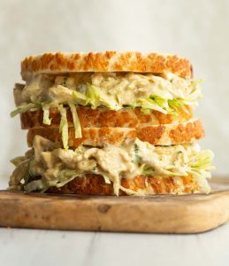 two coronation chicken sandwiches stacked on a wooden board