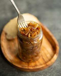caramelized onion in jar on wooden board with silver fork sticking in