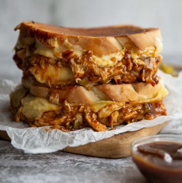 two sandwiches stacked on wooden board with cheese and chicken spilling out