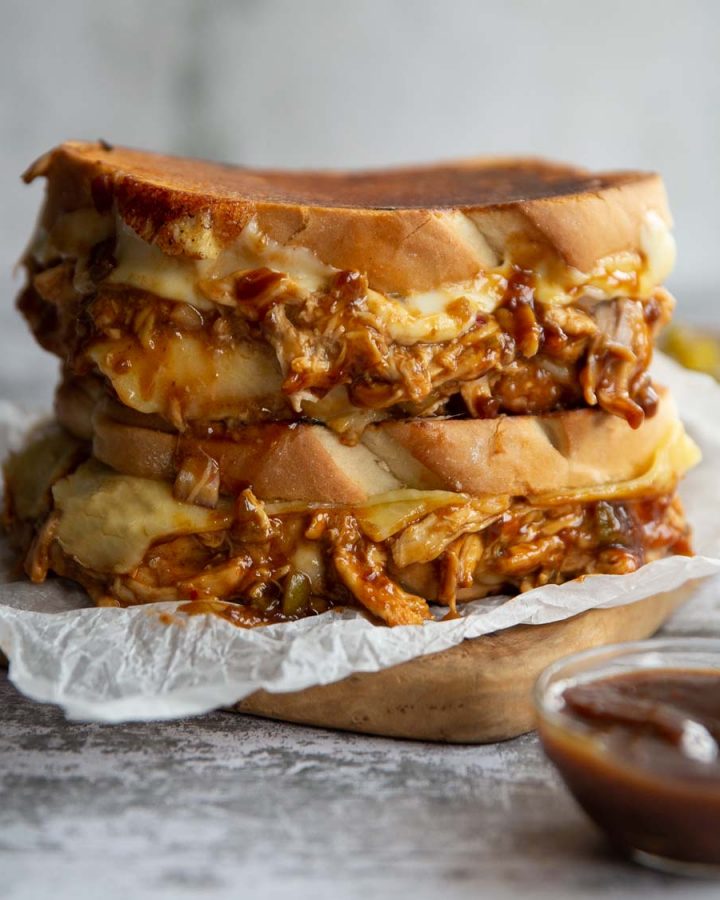two sandwiches stacked on wooden board with cheese and chicken spilling out