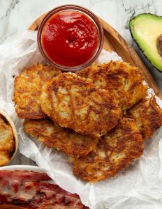 over head shot of hash browns surrounded by avocado, bacon and ketchup