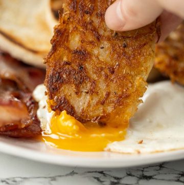 dunking a hash brown into a sunny side up fried egg with yolk pouring out