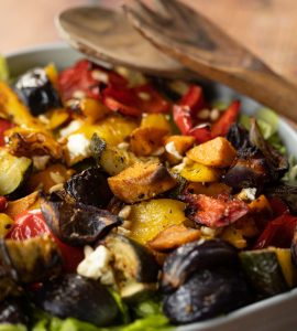 close up shot of salad in bowl with salad tosser resting on dish in background