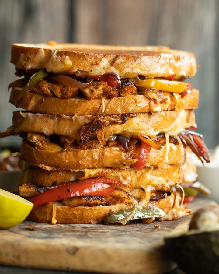 3 sandwiches stacked on each other with filling spilling out on wooden board