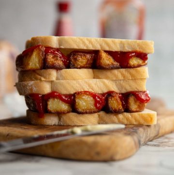 two sandwiches stacked on each other on wooden board with ketchup, vinegar and bread blurred in background
