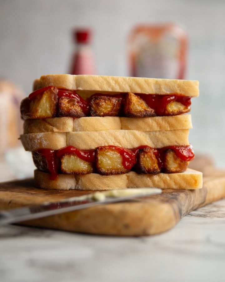two sandwiches stacked on each other on wooden board with ketchup, vinegar and bread blurred in background