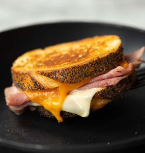 spatula lifting grilled cheese from pan with cheese dripping out