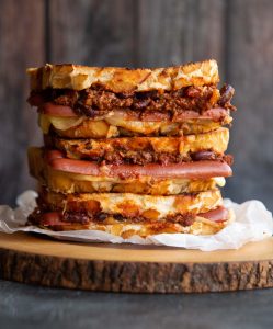 3 sandwiches stacked on each other will chili cheese dogs spilling out