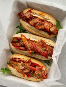 overhead shot of 3 sausage pepper sandwiches in large baking dish garnished with fresh parsley