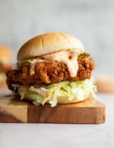 chicken sandwich on wooden board with sauce dripping out