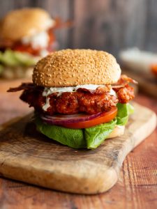 chicken sandwich on wooden board with another sandwich blurred in background
