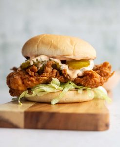 chicken sandwich on wooden board with dip blurred in background