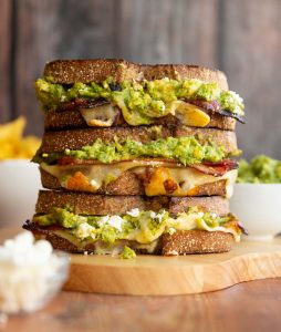 3 sandwiches stacked on each other with guac, cotija and chips blurred in background