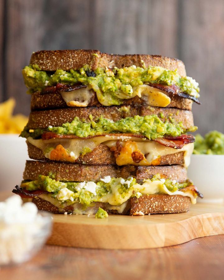3 sandwiches stacked on each other with guac, cotija and chips blurred in background