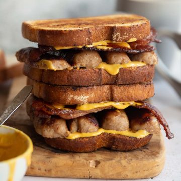 two sandwiches stacked on each other on wooden board with yellow sauce dripping out