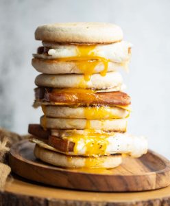 3 sandwiches stacked on each other on wooden board with yolk dripping out