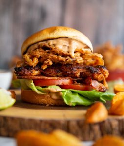 close up shot of chicken sandwich on wooden serving board with sauce dripping out