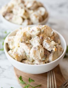 potato salad served in small white bowl on wooden board with second bowl blurred in background