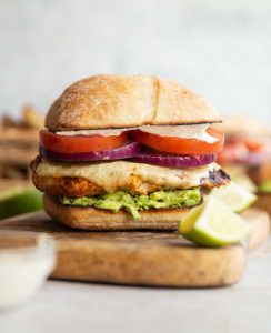chicken avocado sandwich on wooden board with lime and mayo blurred in fornt