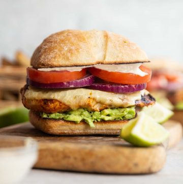 chicken avocado sandwich on wooden board with lime and mayo blurred in fornt
