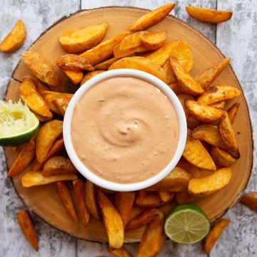 overhead shot of chipotle mayo in white pot surrounded by potato wedges