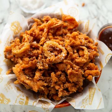 fried onions in wooden bowl with salt and bbq sauce blurred in background