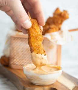 hand dunking in halloumi fry into small glass pot of dip