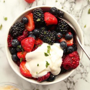 overhead shot of berry fruit salad in small white bowl with yogurt and mint