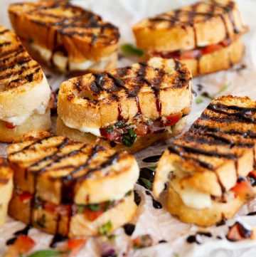 6 bruschetta sandwiches on crumpled parchment paper on wooden board with balsamic glaze