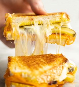 hand lifting up half of sandwich with pickles and cheese falling out