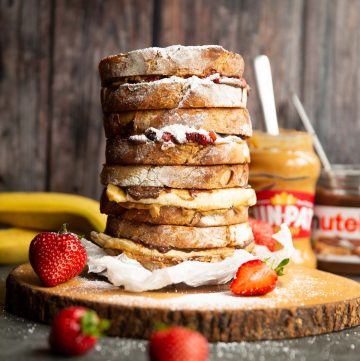 4 sandwiches stacked on each other on wooden board garnished with icing sugar and strawberries