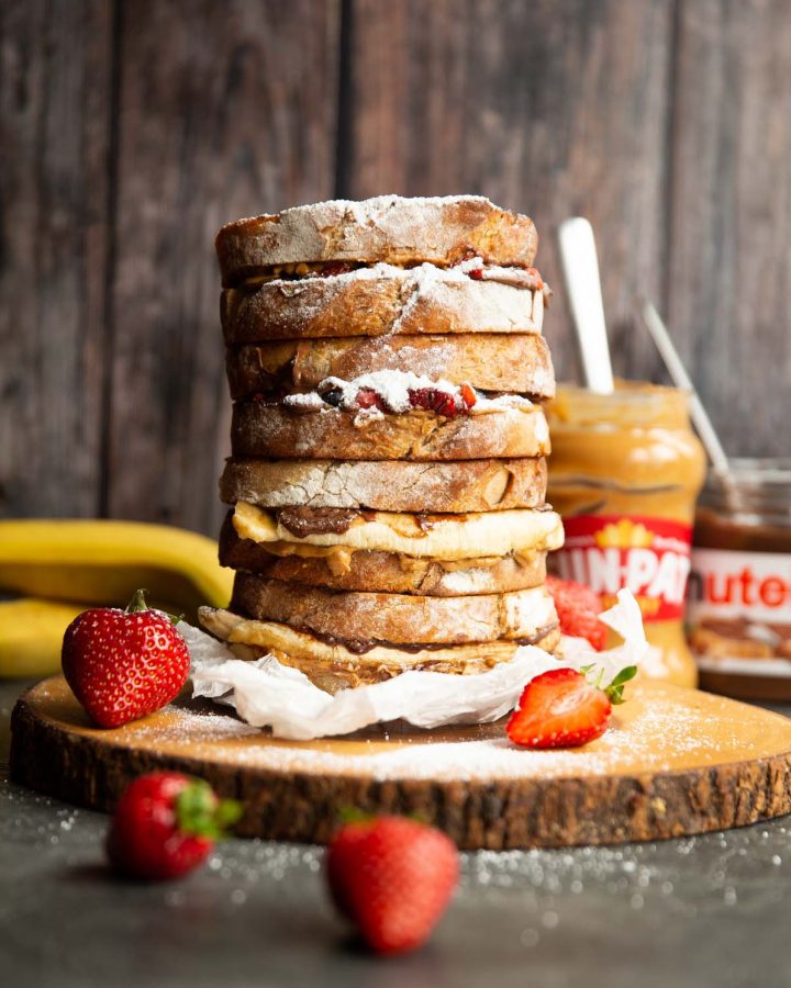 4 sandwiches stacked on each other on wooden board garnished with icing sugar and strawberries