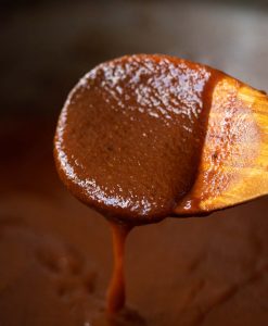 close up shot of bbq sauce dripping off wooden spoon into pot