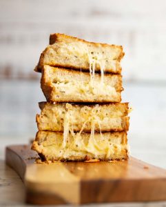 4 sandwich halves stacked on top of each other with cheese dripping out on wooden board