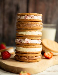 6 cheesecake sandwiches stacked on each other on wooden board with strawberries and milk
