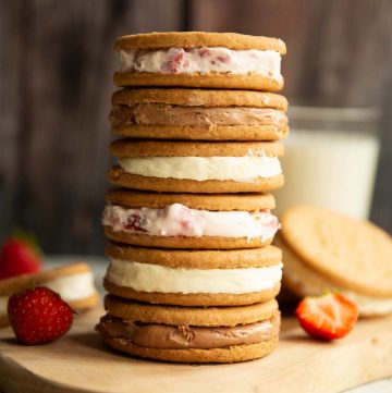 6 cheesecake sandwiches stacked on each other on wooden board with strawberries and milk