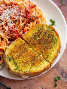 overhead shot of garlic bread grilled cheese on small white plate with tomato spaghetti