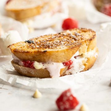 sandwich on crumpled parchment paper surrounded by raspberries and white chocolate chips